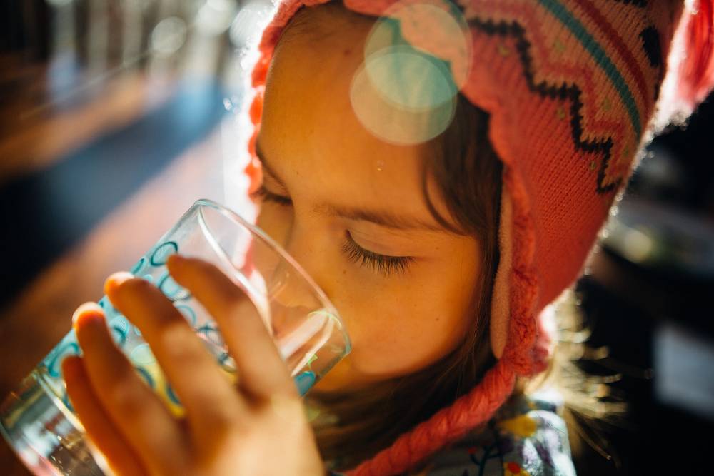 una bambina beve acqua da un bicchiere